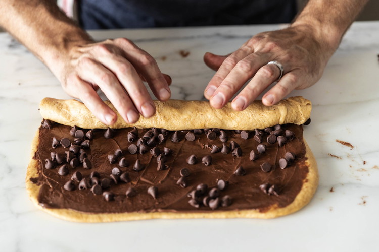 Image of Sprinkle 1⁄2 cup chocolate chips (90 grams) evenly over the spread. Starting from one long side, roll the dough tightly into a long log.
