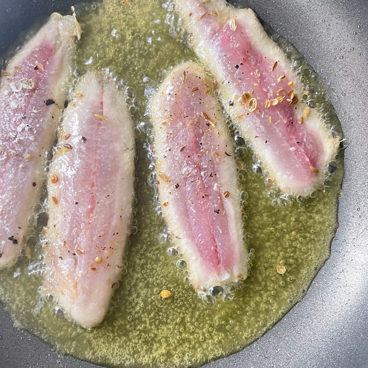 Image of In small batches, lay the seasoned filets skin side down and cook until the skin is blistered, and filets are half cooked.