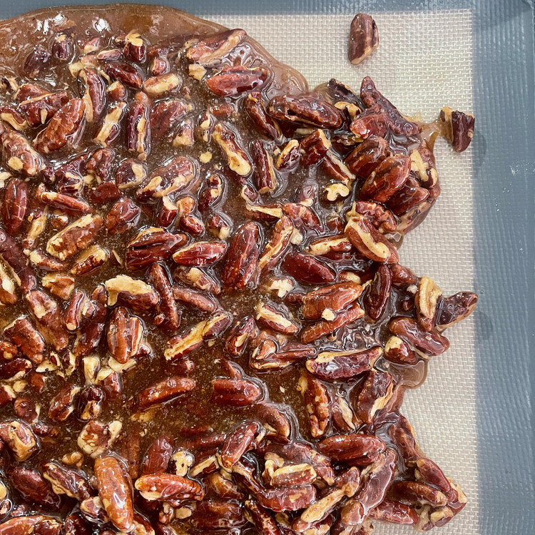 Image of Using a heat resistant spatula or spoon, stir in the Sri Lanka and pecans and pour the mixture out immediately onto the prepared baking sheet to cool.