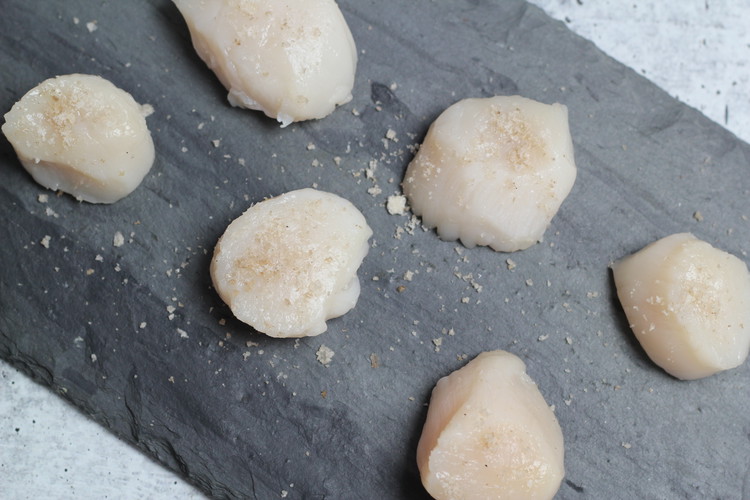 Image of While the pan is heating up, sprinkle one side of your scallops generously with Upta Camp smoked sea salt and some fresh cracked black pepper