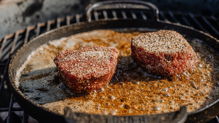 Image of In a heated cast-iron skillet over direct heat, melt butter and add the filets to the skillet to begin searing. Cook for 3 minutes on each side.