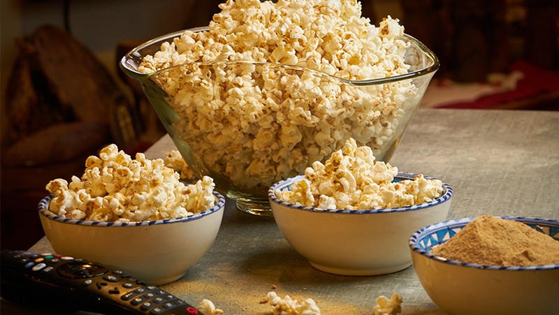 Three small bowls of popcorn and one large one on a table with a remote.
