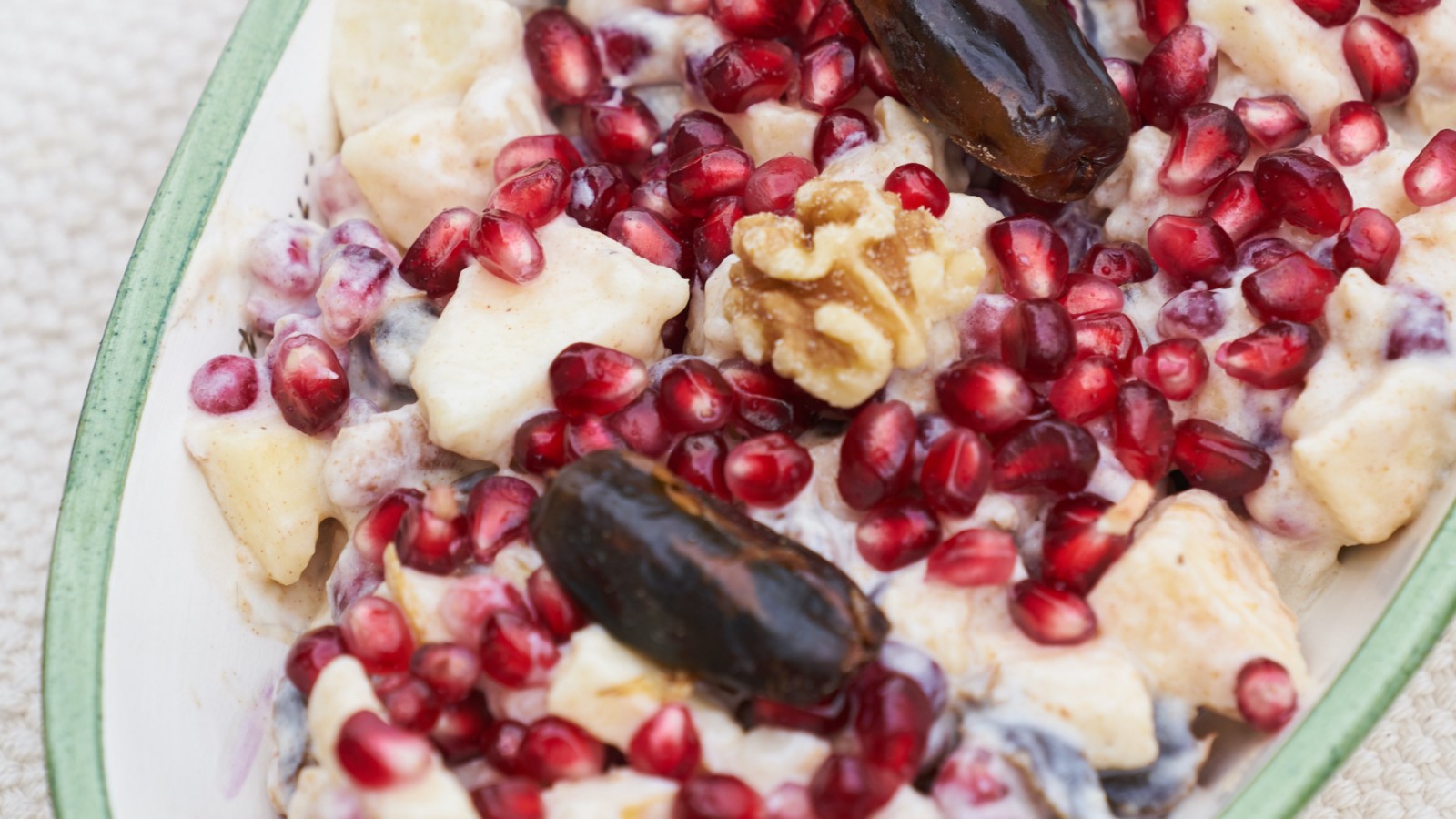 A bowl of fresh fruit, polmegranite, dates, and walnuts.