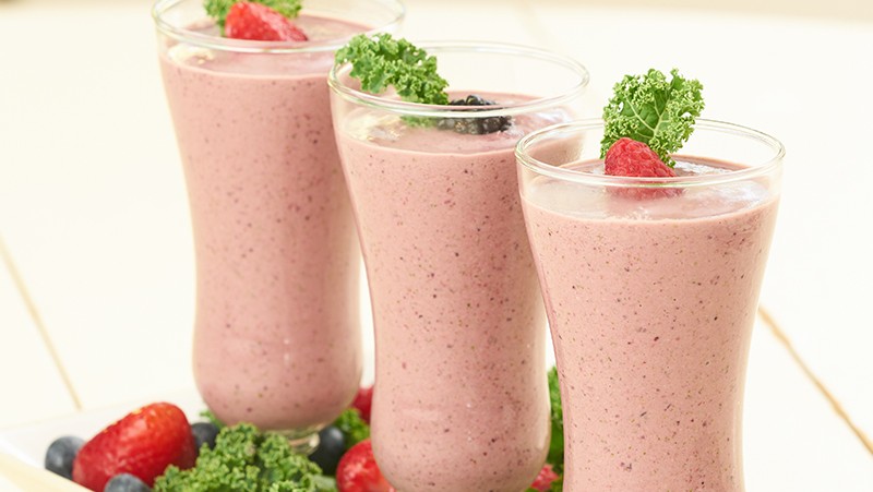 Three cups filled with strawberry banana smoothie and date sugar. Recipe. Topped with kale and berries.
