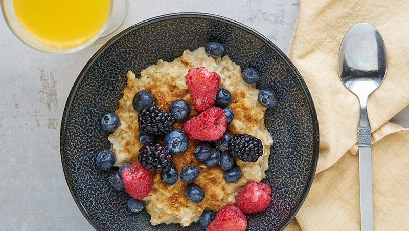 Bowl of oatmeal topped berries and Purdate date sugar. A glass of orange juice and a spoon.