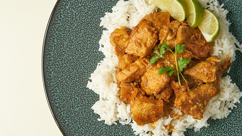 Plate with white rice on the bottom, topped with orange chicken, three limes, and cilantro.