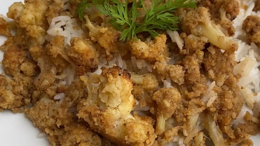 Bowl of Sesame Cauliflower with lemons and topped with herbs.