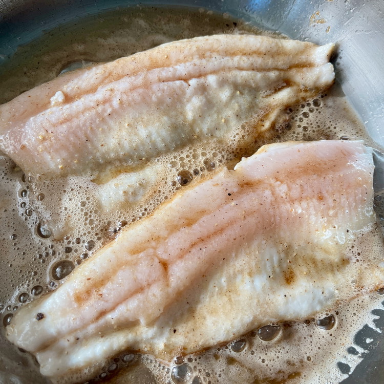Image of When the skin is crispy and the flesh is half cooked, add the butter and gently swirl the pan to slide some butter under the fish and help the butter brown evenly.