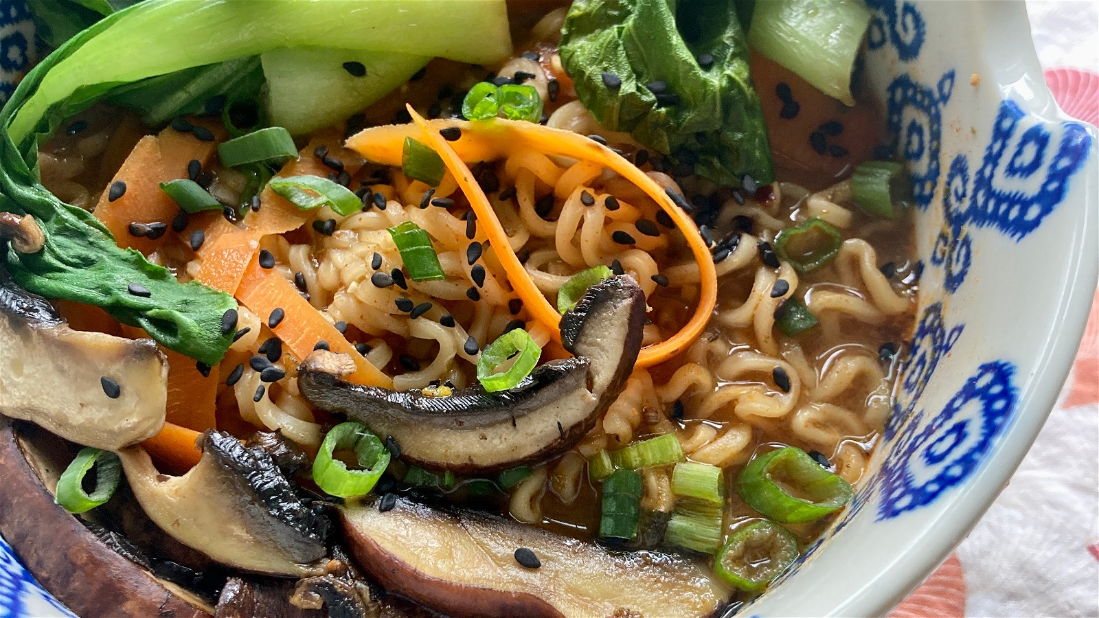 A bowl with blue decorations filled with ramen noodles, carrots, mushrooms, and baby bok choy with Well Seasoned Table Thai Red Curry Seasoning.