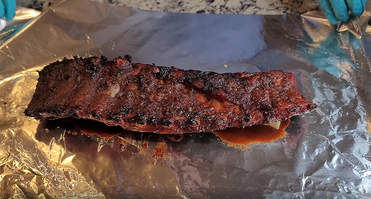 Image of At the 3 hour mark, the ribs should ready to wrap. Take a sheet of tinfoil that can wrap the entire rack of ribs, spread some pickled jalapeno brine on the center of it, along with 4 pads of butter...