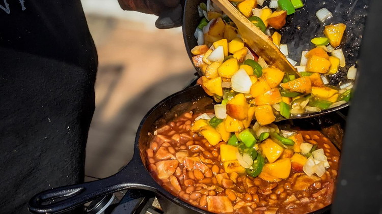 Image of Pour skillet full of peaches, onion, pepper, garlic, brown sugar, and bourbon into the pot and stir.