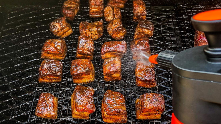 Image of After 2 hours, spritz the pork belly with apple juice and check the internal temperature of a few of your pork belly cubes. Once they reach 165ºF, transfer them to an aluminum pan.