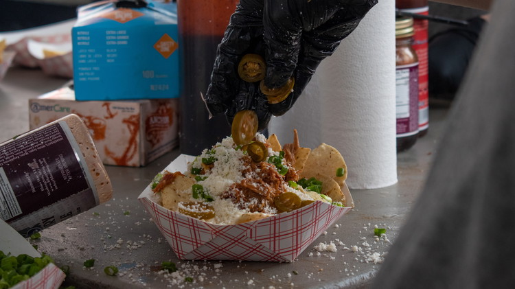 Image of Load up a plate of chips with queso, pork, pickled onions, jalapenos, and green onion. 