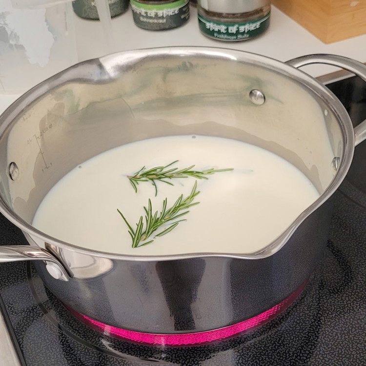 Image of Zuerst kochst du die Milch mit dem Rosmarin auf. Vom Herd nehmen, beiseite stellen. Die wird später für den Vanillepudding benötigt. Durch das Beiseitestellen kann der Rosmarin sein Aroma gut an die Milch abgeben.