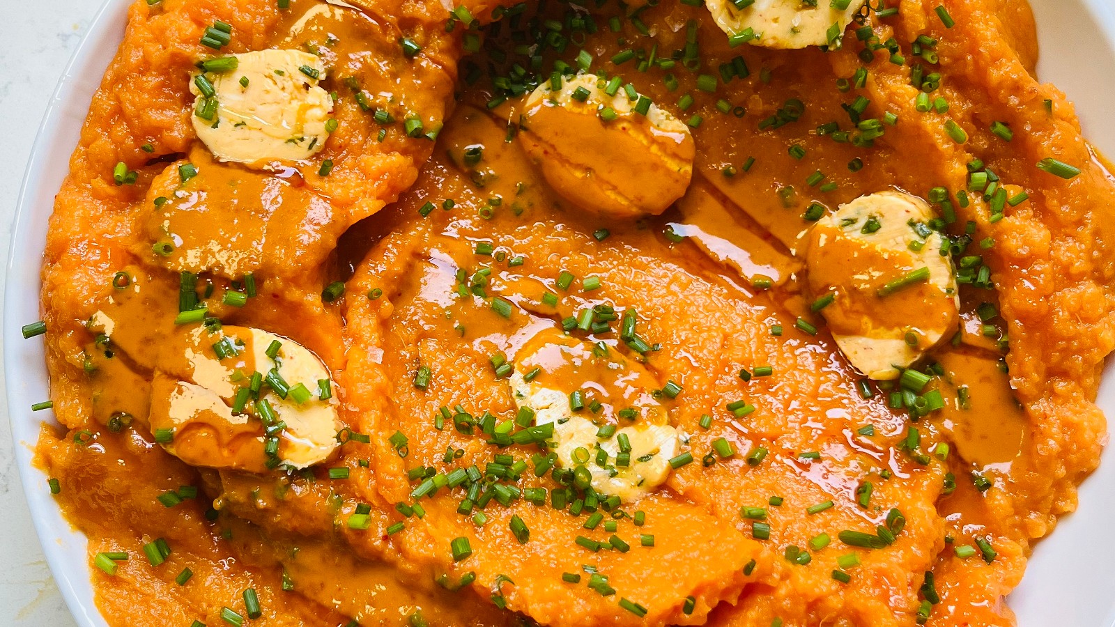 mashed sweet potato in a white dish topped with chili lime butter and chives