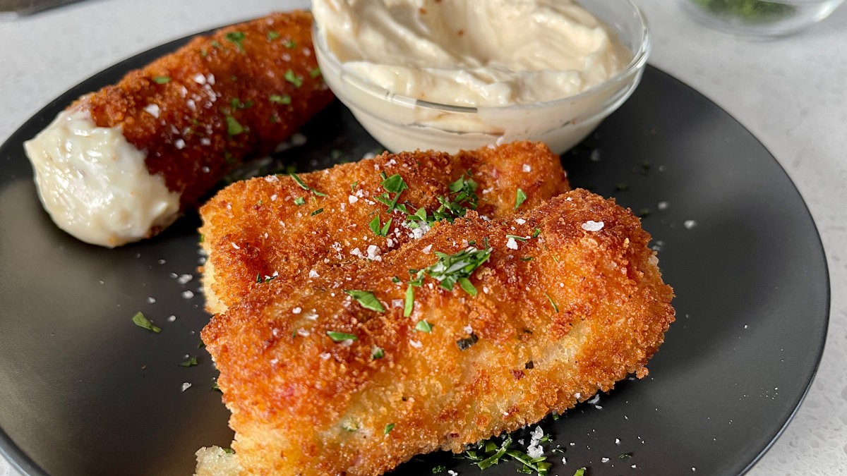 Image of golden brown croquette with creamy garlic sauce drizzled over the top