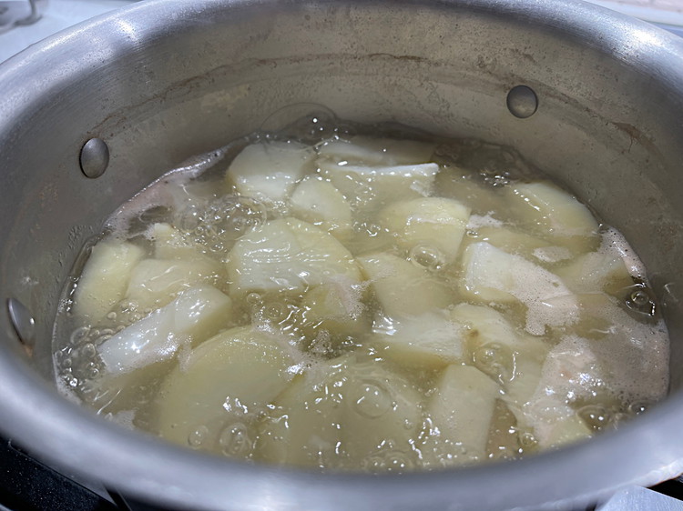 Image of Roughly dice up your peeled potatoes and add them to a pot and cover with water. Add a few twists of rock salt and cook at medium heat until you can push a fork through them without much resistance