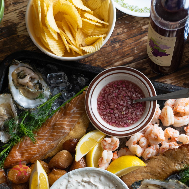 Image of To make the marcuterie board, place an even layer of ice on a large, shallow platter. Arrange salmon, scallops, shrimp and oysters on the platter.