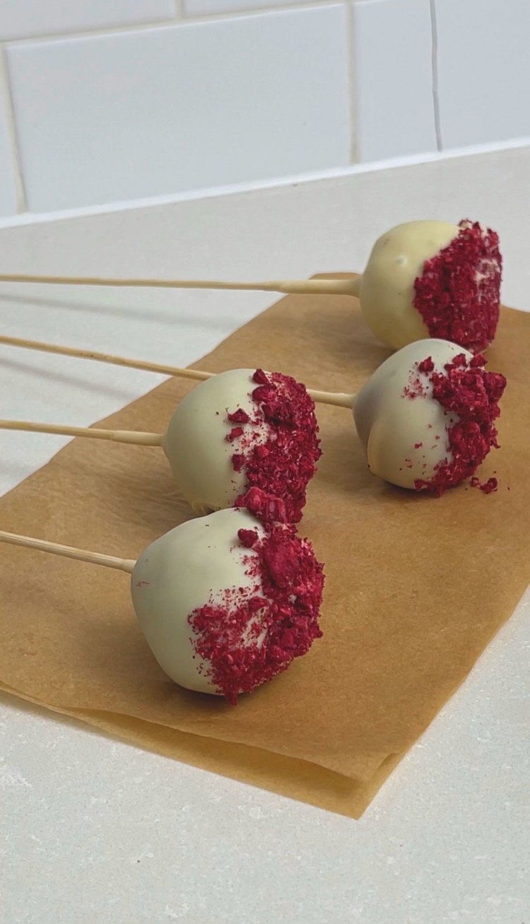Image of Allow the chocolate to set on the sticks. Then dip the balls one at a time into the chocolate glaze. Allow to drip off a little, decorate with freeze-dried raspberries and then carefully place upright into a styrofoam block.