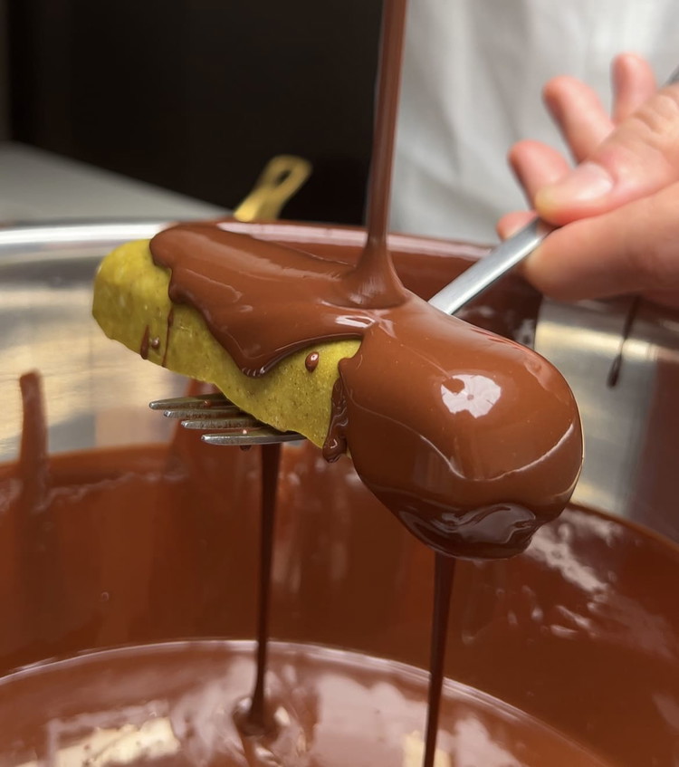 Image of Then, using a fork placed underneath, dip every piece into the hot dark chocolate, covering it completely. Then place your chocolate-covered pieces on your lined cookie sheet.