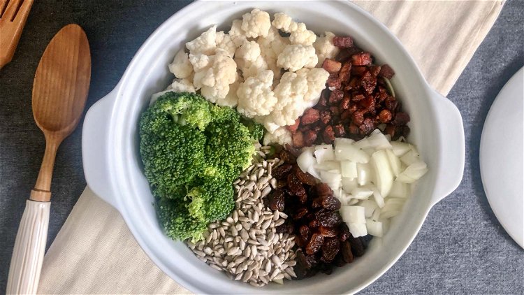 Image of In a large bowl mix broccoli, cauliflower, bacon, raisins, and...