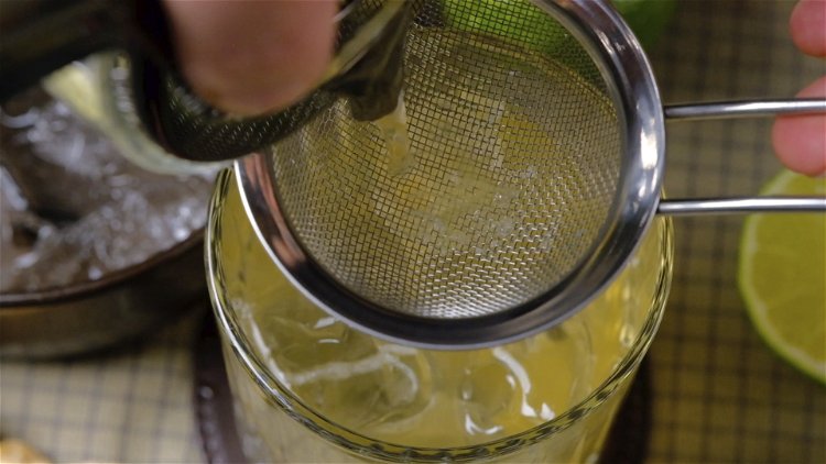 Image of Der Drink wird in ein Glas mit Eiswürfeln abgeseiht.