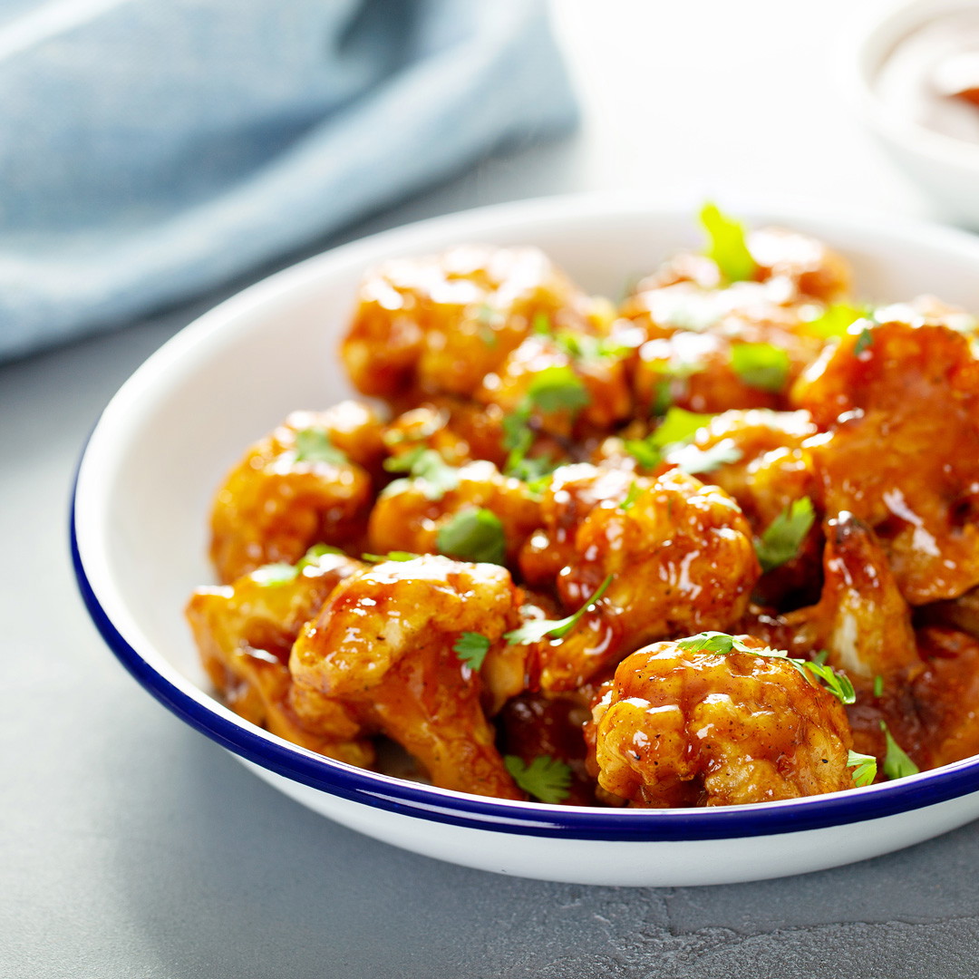 A bowl of buffalo cauliflower bites garnished with scallions.