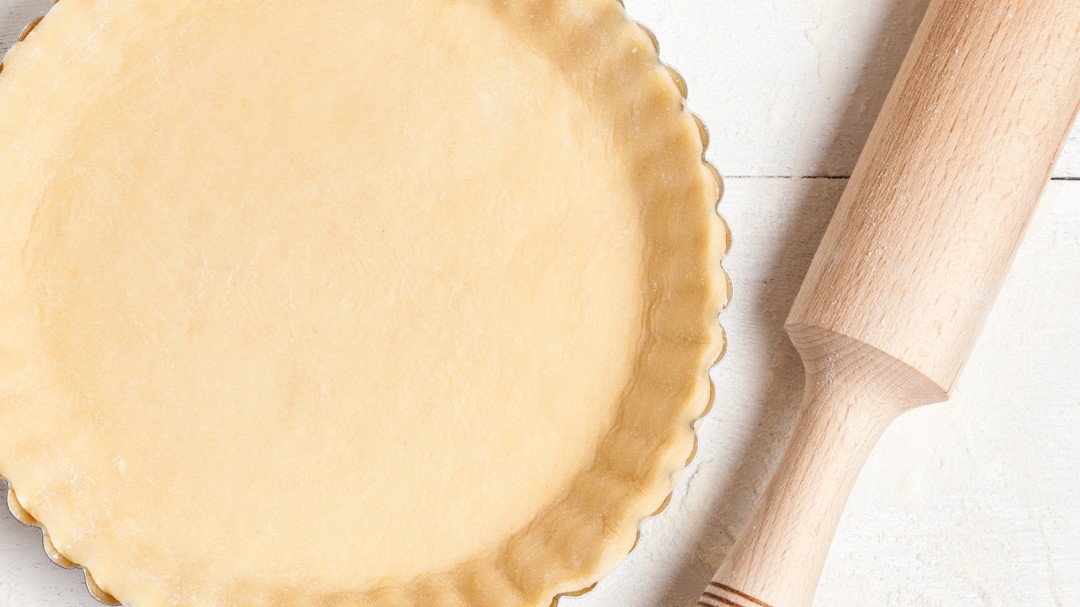 A rolling pin sitting next to a pie dish filled with pie crust.