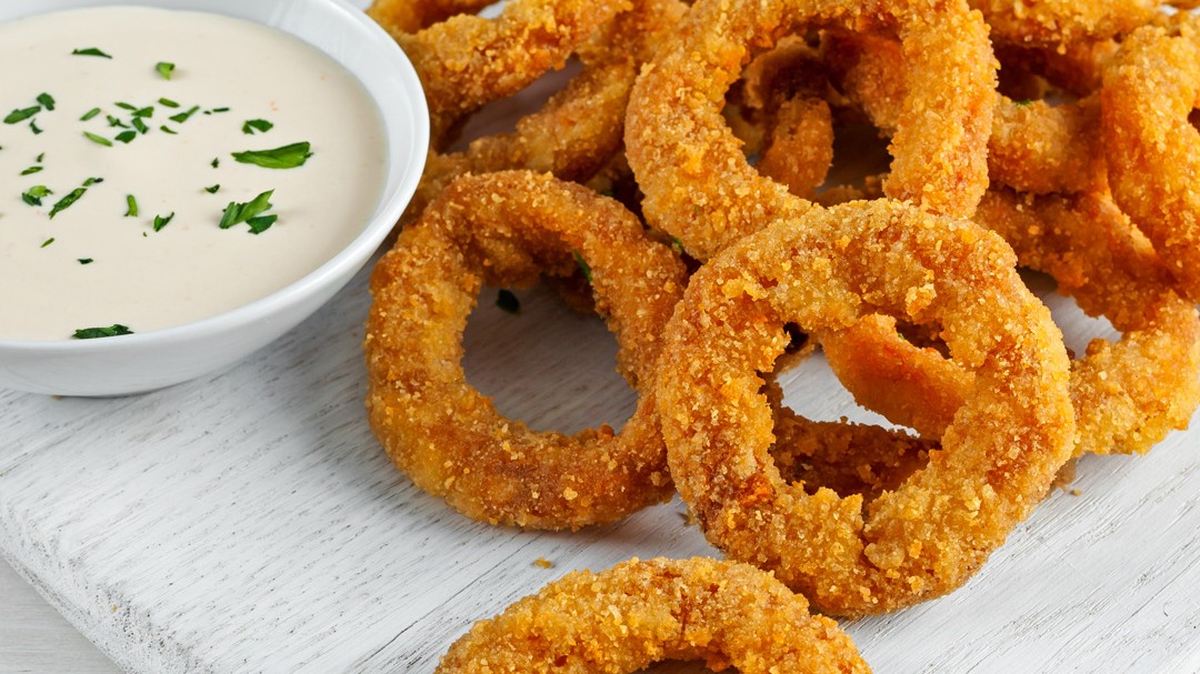 Crispy onion rings and a dipping sauce on a wooden plate.