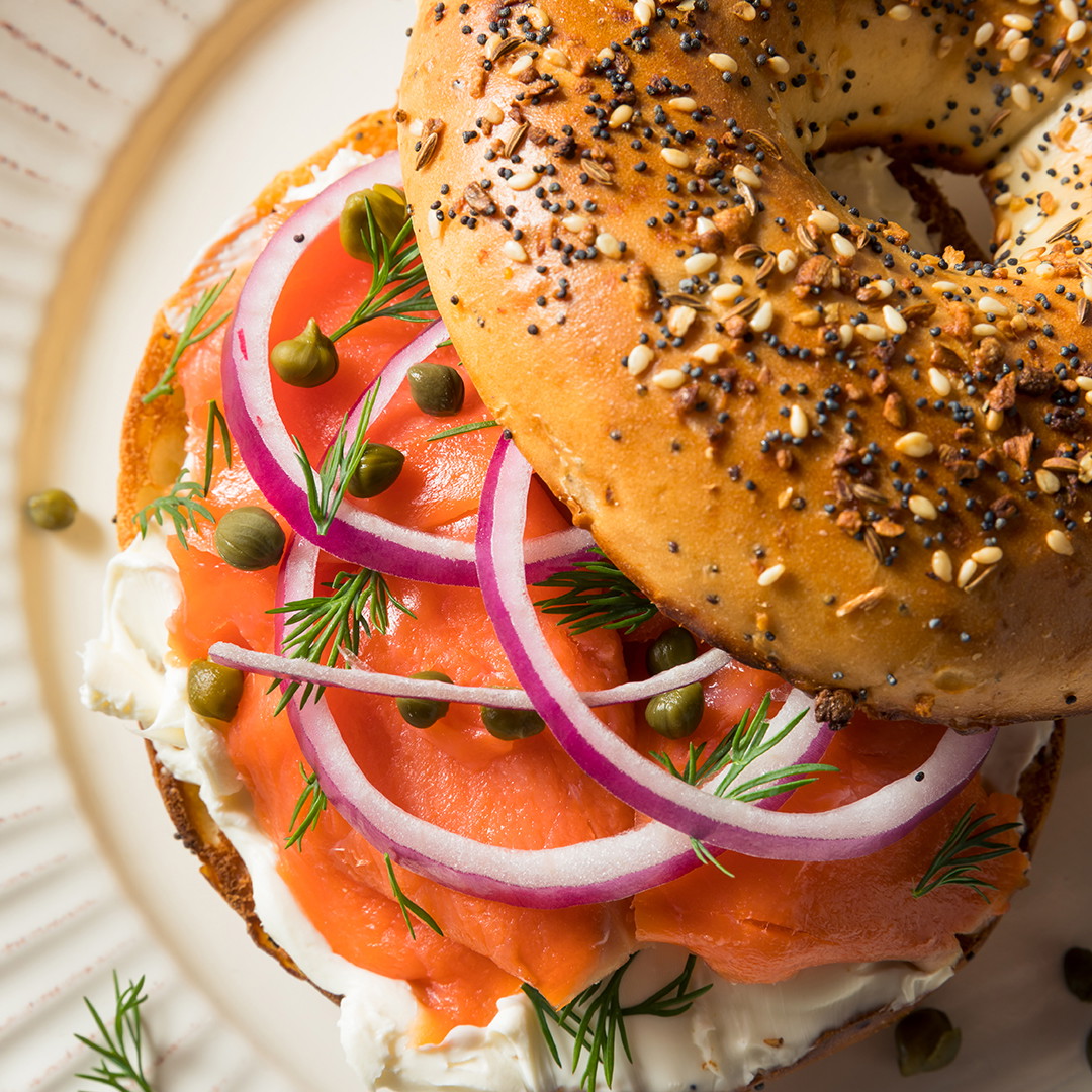 Un bagel everything con queso crema, salmón, alcaparras, cebollas moradas y eneldo en un plato blanco.