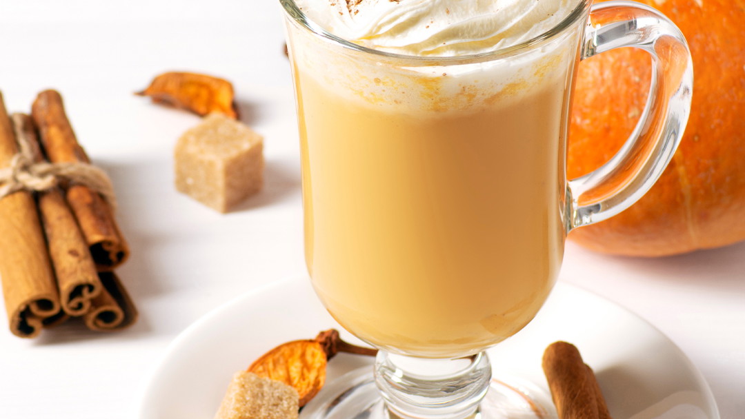 Pumpkin spice latte in a tall clear mug topped with whipped cream and a sprinkle of pumpkin pie spice.