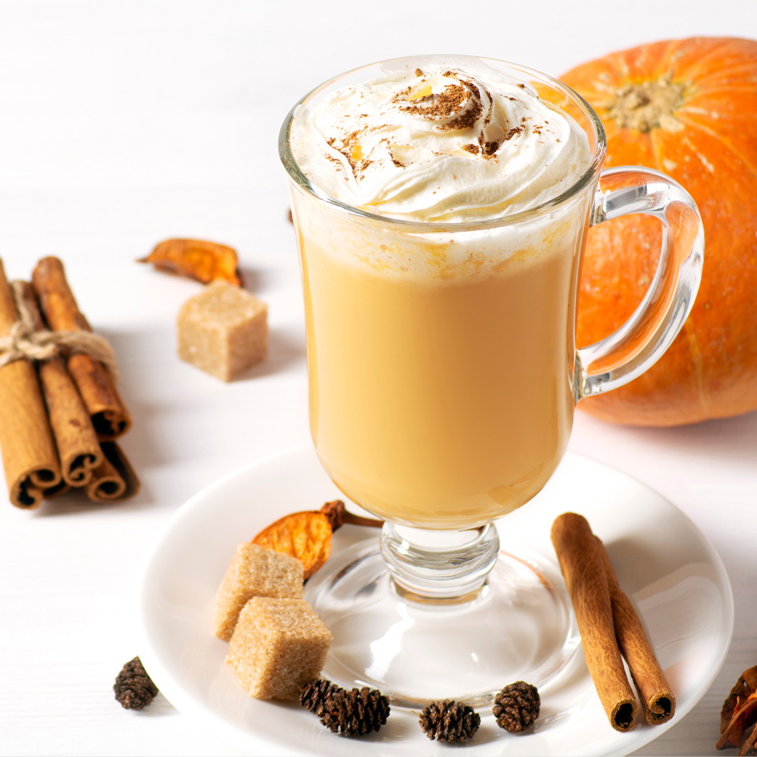 Latte de calabaza y especias en una taza alta transparente con crema batida y una pizca de especias de calabaza.