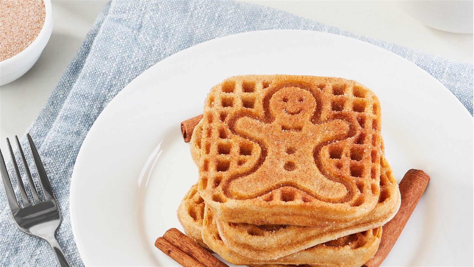 Four snickerdoodle waffles coated with cinnamon sugar stacked on a white plate.