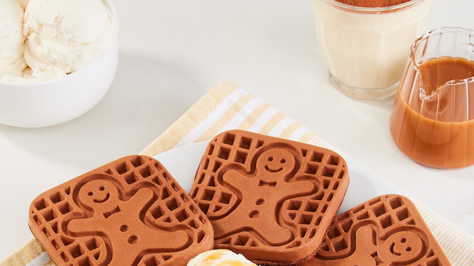Four chocolate eggnog waffles with a gingerman print on a white plate topped with one scoop of vanilla ice cream and caramel drizzle.