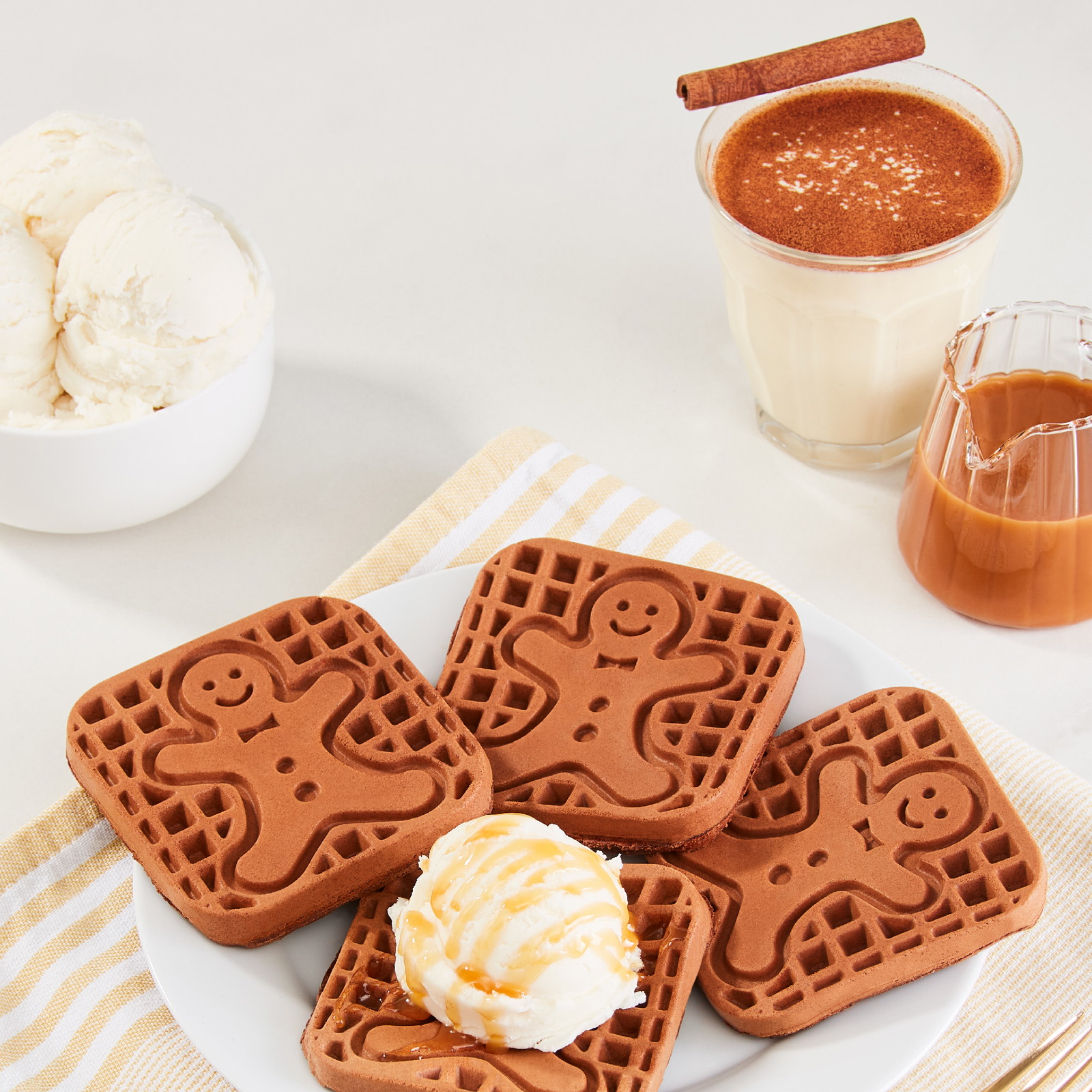 Four chocolate eggnog waffles with a gingerman print on a white plate topped with one scoop of vanilla ice cream and caramel drizzle.
