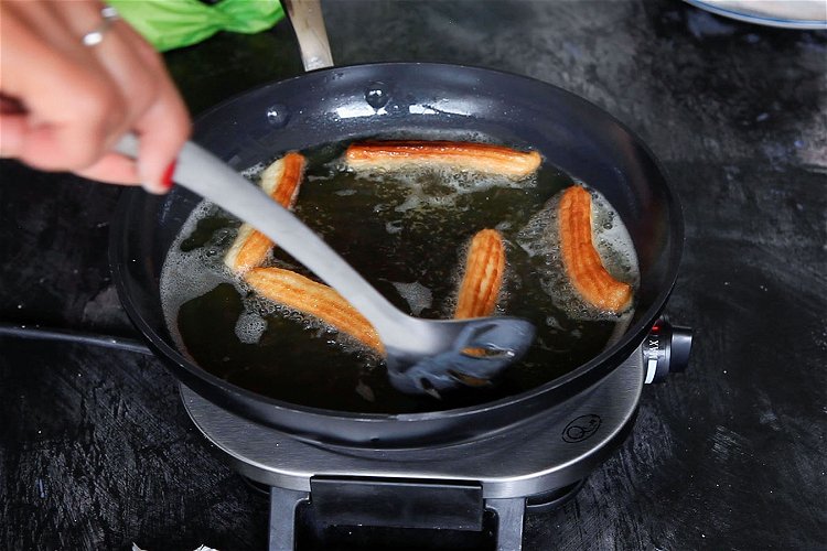 Image of Using a slotted, spoon pop the churros into the oil....
