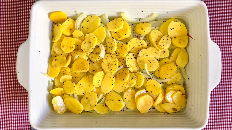 Image of Place sliced onions and thinly sliced potatoes in a buttered 9x13 baking dish. Season with salt and pepper.