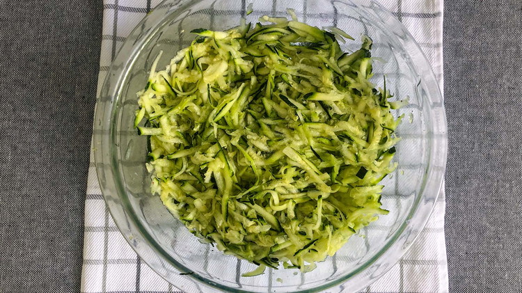 Image of Start by preheating the oven to 350°. Grate zucchini and add salt to draw out extra moisture. Pat dry with a towel, cheesecloth, or drain in a colander.