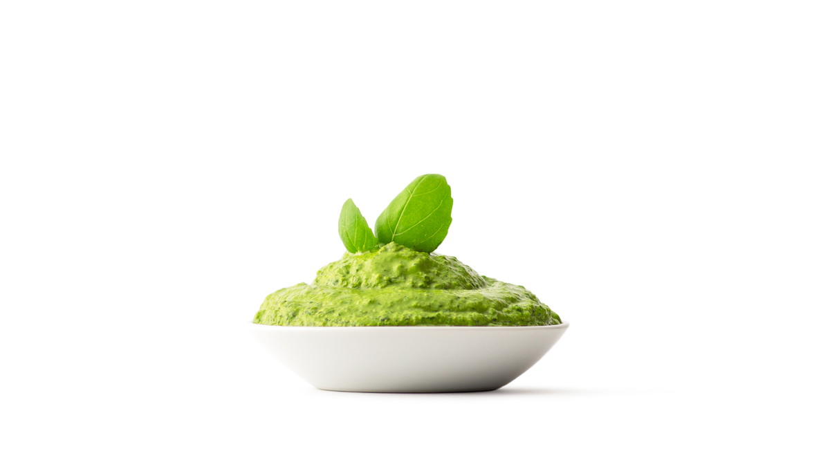 sunflower seed pesto with two basil leaves sticking out of the top in a small white dish