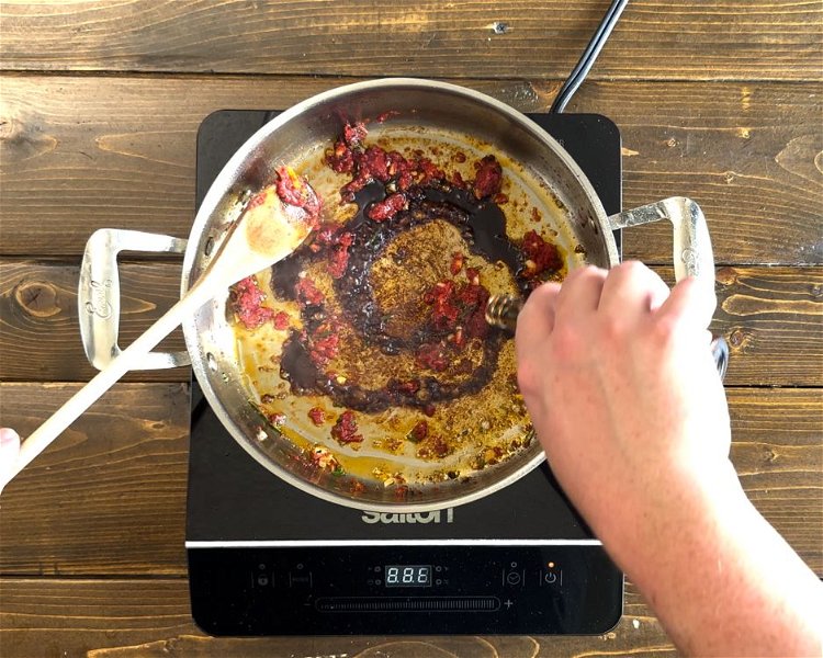 Image of Stir garlic, rosemary, and tomato paste into drippings in skillet....
