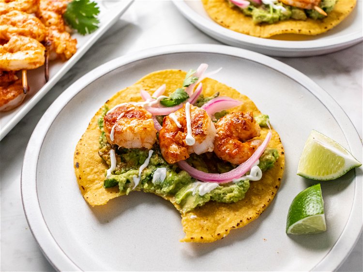 Image of Spread guacamole on tostadas and top with shrimp, pickled red...