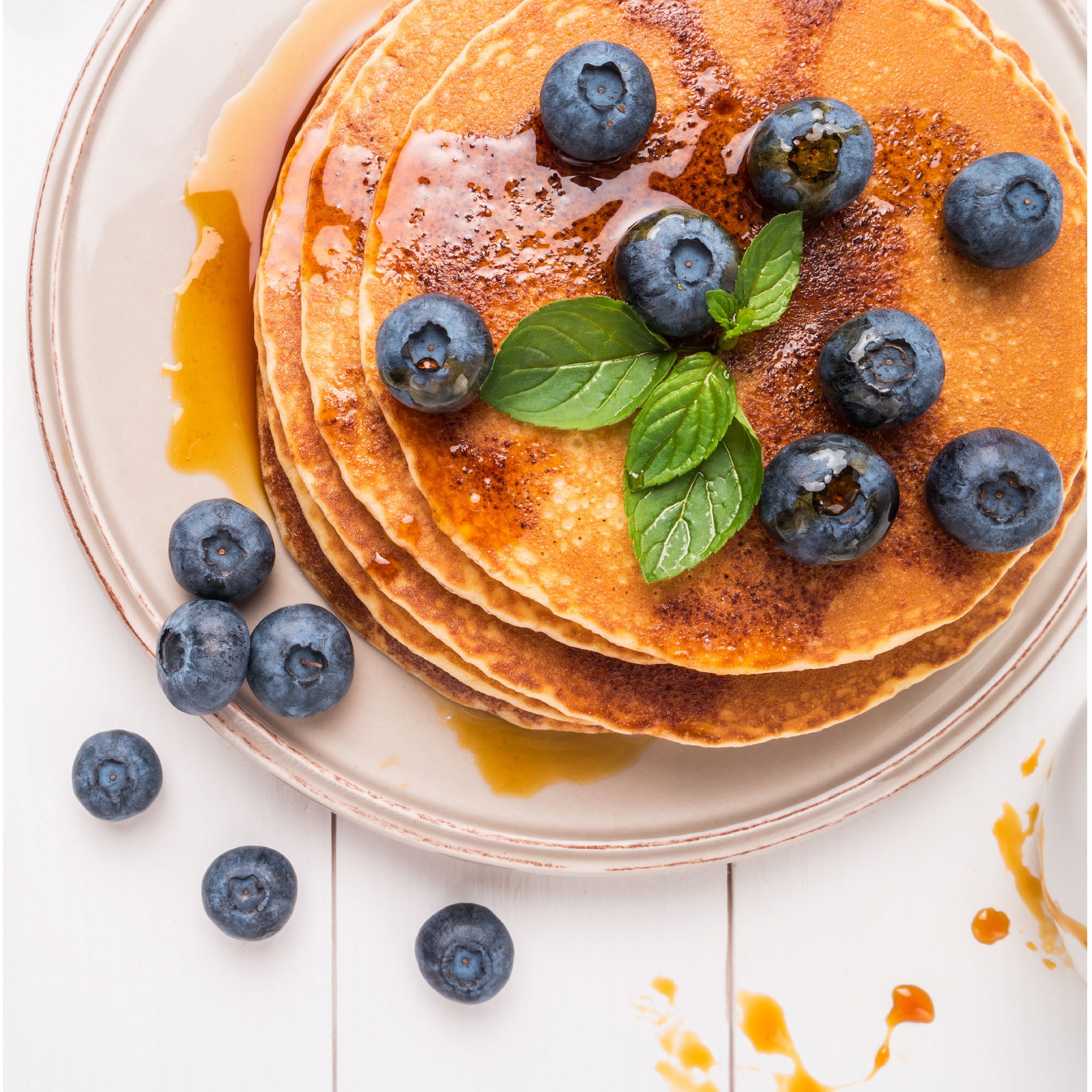 Top down view of a plate of pancakes topped with syrup and blueberries on a marble countertop.