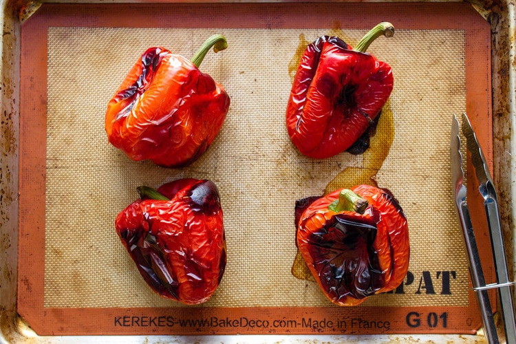 Image of Place the peppers on the baking sheet and grill them until their skins are approximately 90% blackened. Flip them over and grill until they are 90% blackened on all sides.