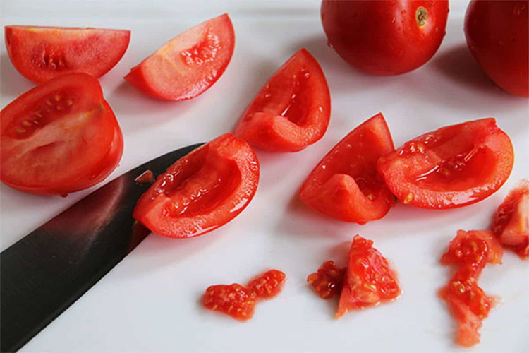 Image of Cut Roma tomatoes into quarters and remove the seeds using a sharp knife, skilfully slicing away the seeds from the flesh.