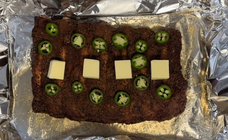 Image of After three hours, put them in tinfoil with the crème soda, top with butter, and jalapeno slices. Wrap tightly and return to the smoker for another two hours allowing the crème soda and jalapeno to work their magic, infusing the...