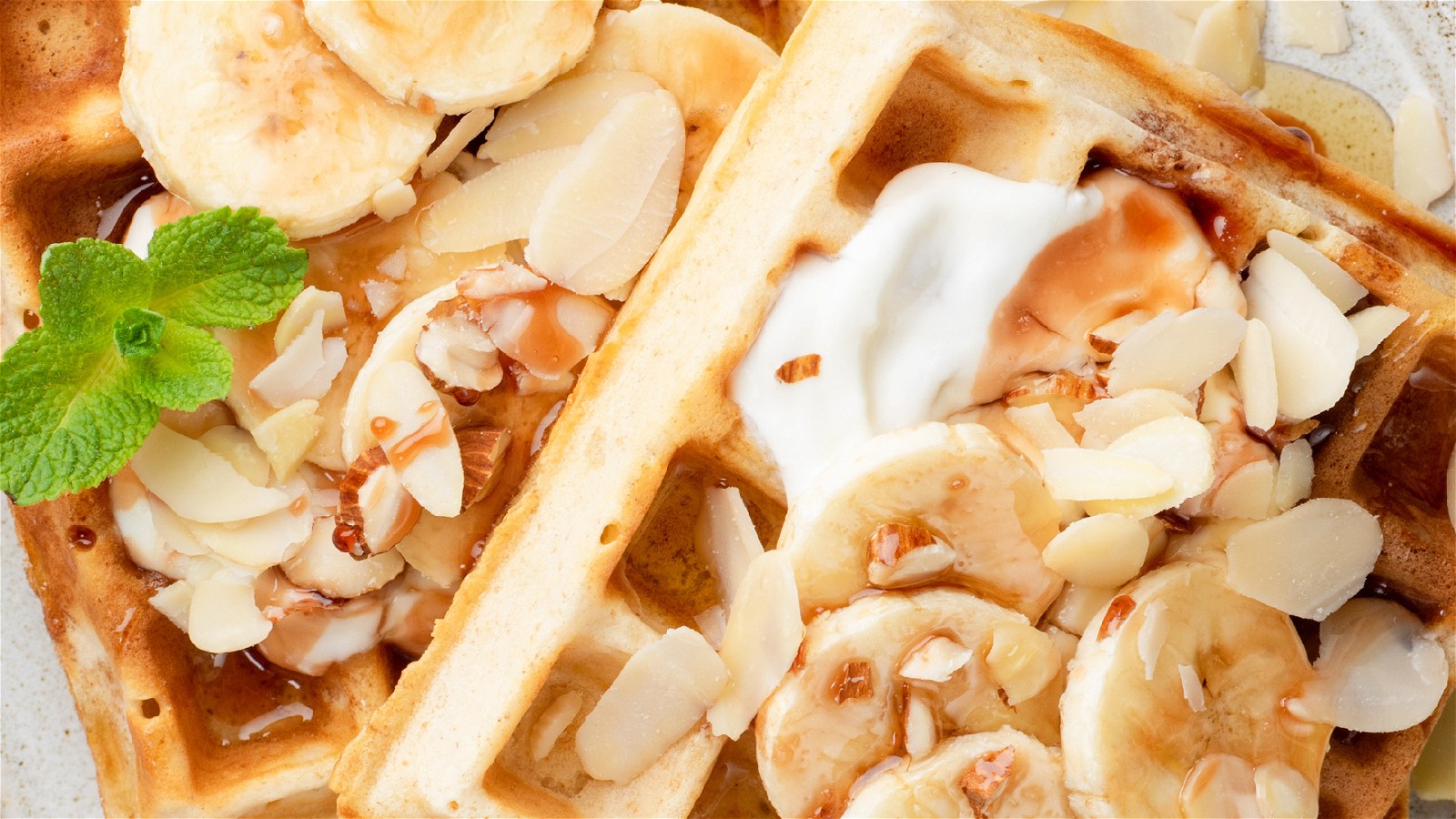Banana bread waffles topped with banana slices, sliced almonds, and honey.