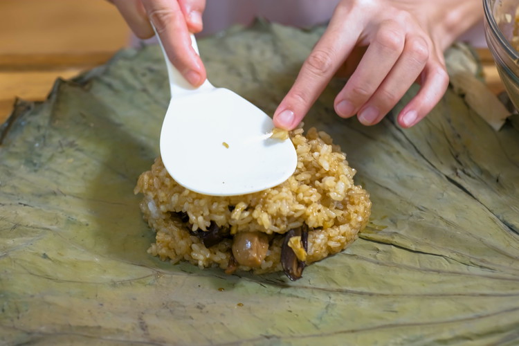 Image of To wrap the lo mai gai, use 1/3 cup of the glutinous rice to form a rectangle bed on the lotus leaf. Then I add the chicken, mushroom, sausage, and shrimp on top of the rice bed. Cover them with...