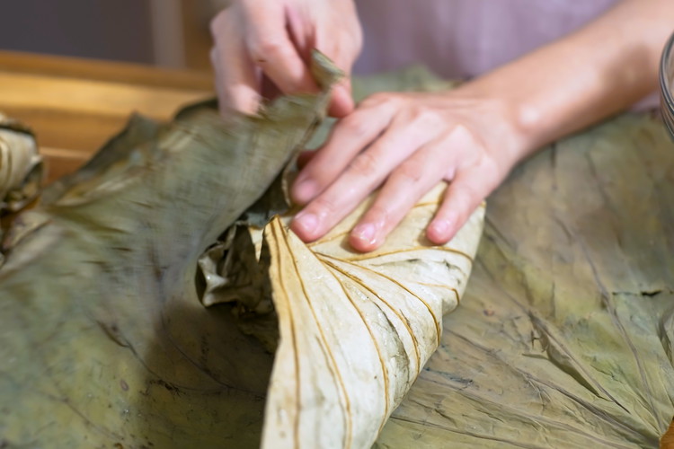 Image of Lift up one side of the leave and fold it over the rice. Tuck it tight, then fold two sides to the middle. Roll over the rest of the leaf like making an envelope. Sometimes lotus leaves will have some...