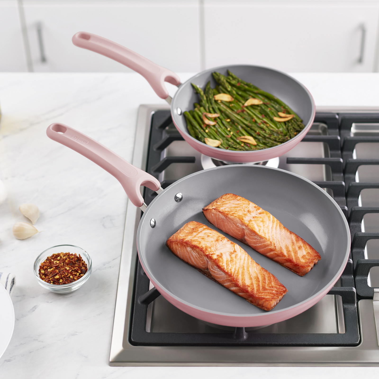 Deux poêles sur une cuisinière, l'une contient deux filets de saumon et l'autre des asperges.