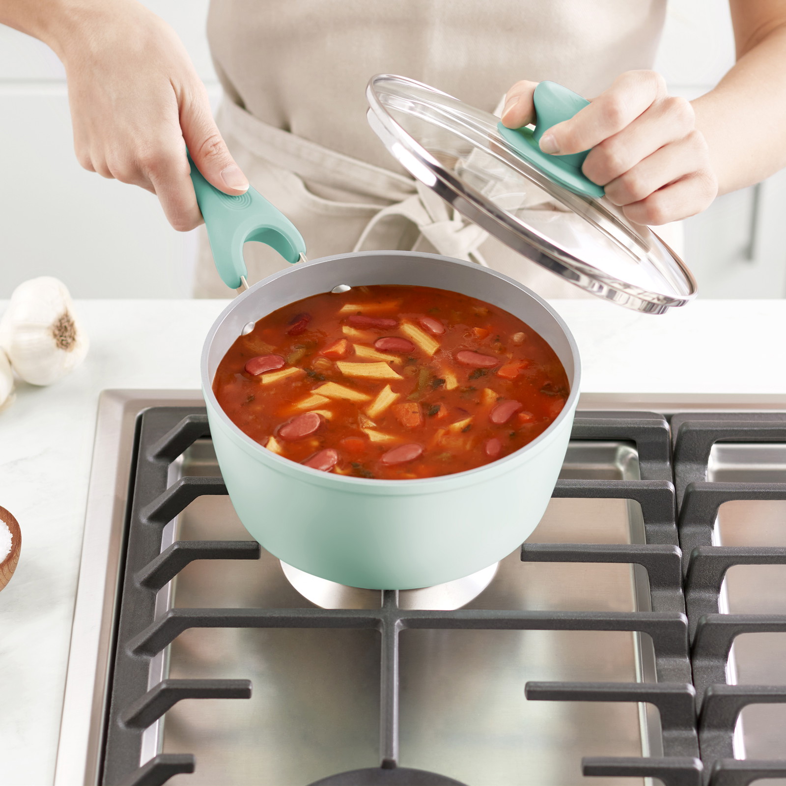 Un homme tient une casserole de soupe et son couvercle sur un brûleur de cuisinière.